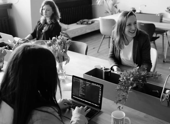 Three people working together on a shared desk with opened laptops